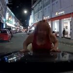 Woman leaning on car bonnet in Bugis dashcam still