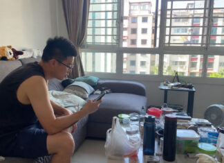 A man in a Singapore HDB living room looking at a smartphone