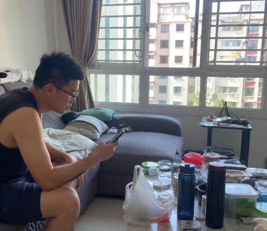 A man in a Singapore HDB living room looking at a smartphone
