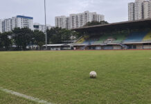 A football on the pitch at a Singapore stadium with HDB blocks behind the stands