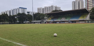 A football on the pitch at a Singapore stadium with HDB blocks behind the stands