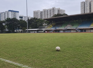 A football on the pitch at a Singapore stadium with HDB blocks behind the stands