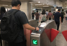 A commuter tapping a card at a Singapore MRT fare gate in the morning
