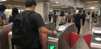 A commuter tapping a card at a Singapore MRT fare gate in the morning