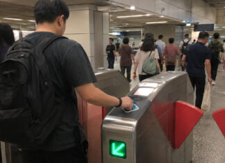A commuter tapping a card at a Singapore MRT fare gate in the morning