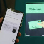 iPhone showing Apple Pay Express Travel Card settings held in front of a Singapore MRT fare gantry