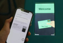 iPhone showing Apple Pay Express Travel Card settings held in front of a Singapore MRT fare gantry