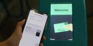 iPhone showing Apple Pay Express Travel Card settings held in front of a Singapore MRT fare gantry