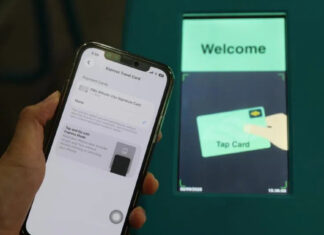 iPhone showing Apple Pay Express Travel Card settings held in front of a Singapore MRT fare gantry