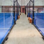 Empty indoor padel courts with blue turf and glass walls, non-literal stock for a sports-gear investment dispute