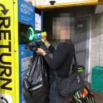 A man returning a bottle at a Return Right BCRS machine while holding a bag of collected cans