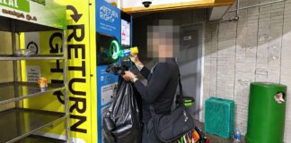 A man returning a bottle at a Return Right BCRS machine while holding a bag of collected cans