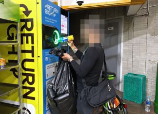 A man returning a bottle at a Return Right BCRS machine while holding a bag of collected cans