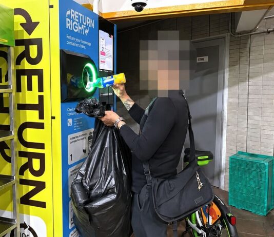 A man returning a bottle at a Return Right BCRS machine while holding a bag of collected cans