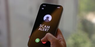 Hand holding a smartphone showing a SCAM ALERT incoming-call screen for a Harvey Norman impersonation scam advisory
