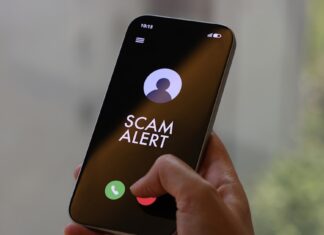 Hand holding a smartphone showing a SCAM ALERT incoming-call screen for a Harvey Norman impersonation scam advisory