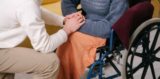 Caregiver holding the hands of a person in a wheelchair (stock photo: Ivan S / Pexels)