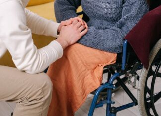 Some Families Could See Disability Care Expenses Fall by Up to 80% by 2028 Caregiver holding the hands of a person in a wheelchair (stock photo: Ivan S / Pexels)