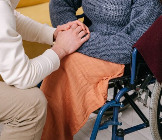 Caregiver holding the hands of a person in a wheelchair (stock photo: Ivan S / Pexels)