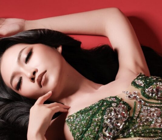 Portrait of a woman in a green beaded gown lying against a red background