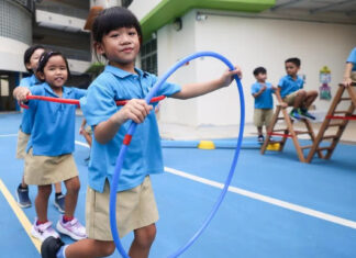 MOE kindergartens to pilot full-day model in 2027, with all centres onboard by 2030 Kindergarten children playing with hoops and climbing frames in a school playground