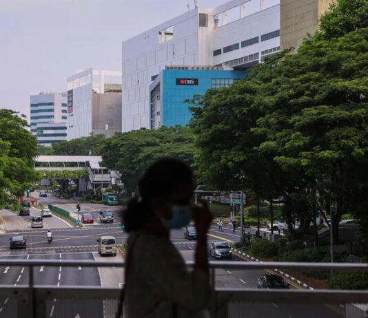 Singapore road and trees seen from a footbridge with commuters in silhouette