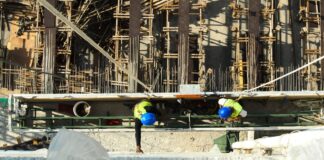 Two construction workers in blue hard hats and safety vests seen from above at a building site (stock photo: Pexels)