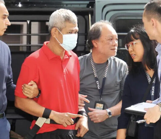 Yishun Landlord Killing Hearing Adjourned Over Differing Psychiatric Reports Affendi Yusoff escorted by police officers beside a police vehicle